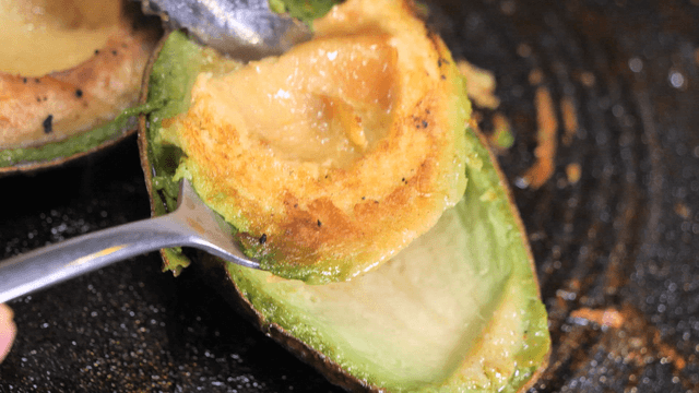 Grilled avocado being scooped with a spoon