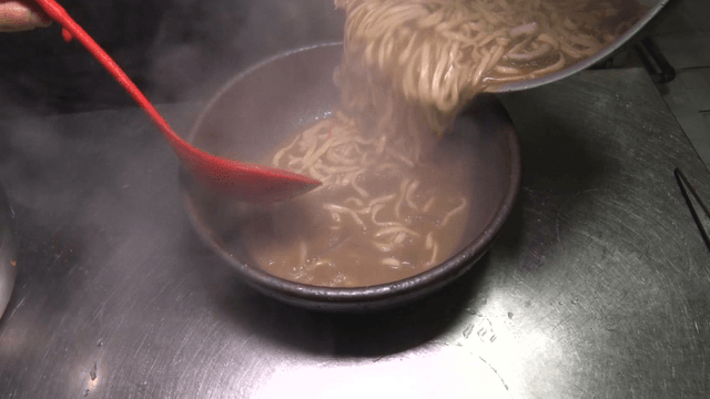 Noodle soup being transferred into a ceramic bowl