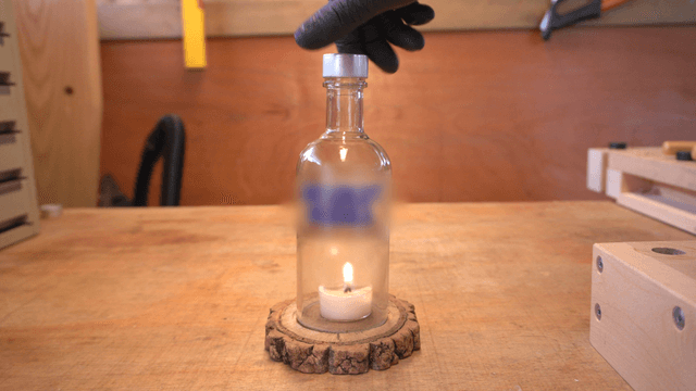 Flickering candle flame beneath a glass jar in workshop
