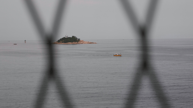 철망 넘어 보이는 등대가 있는 작은 섬과 배