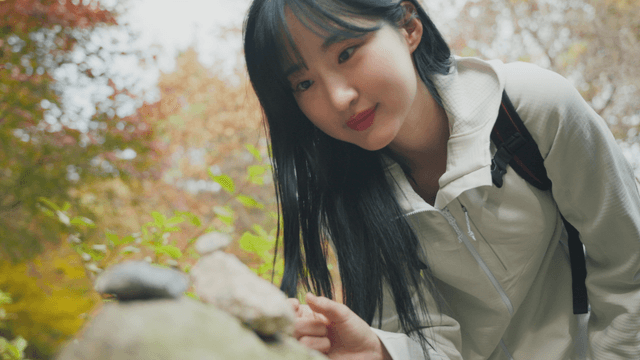 Woman in hiking clothes stacking stones in autumn forest