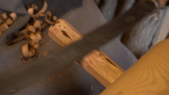 Wood branch being shaped with a drawknife