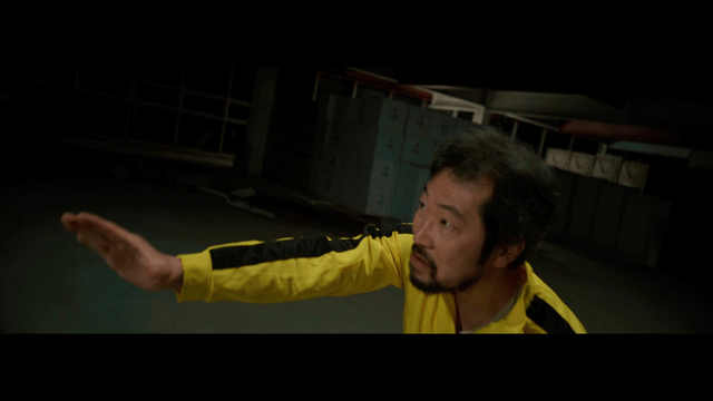 Man in a yellow tracksuit subduing a man in a suit with martial arts