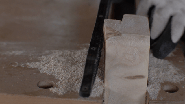 Gloved hands delicately shaping wood with a rasp