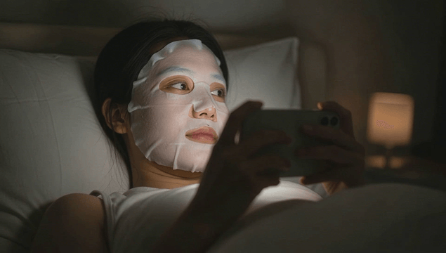 Woman relaxing in bed with a face mask and smartphone