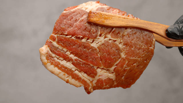 Piece of raw marinated pork held with tongs