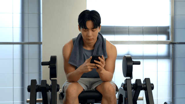 Young man resting on gym equipment while looking at smartphone