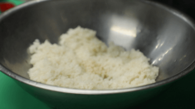 Gloved hand seasoning rice in a bowl