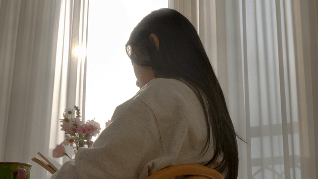 Woman reading book by window with flowers