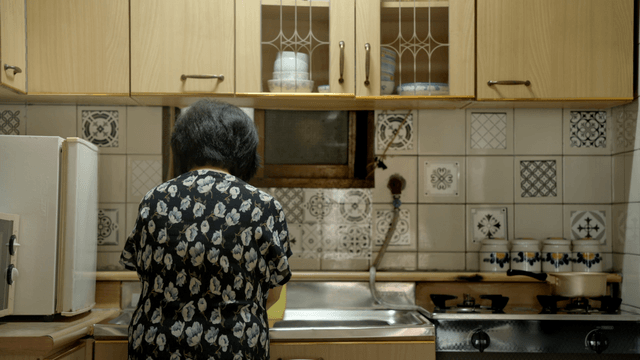Back view of an elderly woman doing the dishes in the kitchen