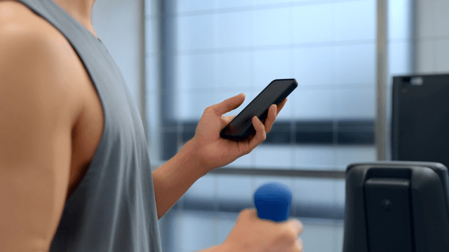 Man using smartphone while lifting a small dumbbell at gym