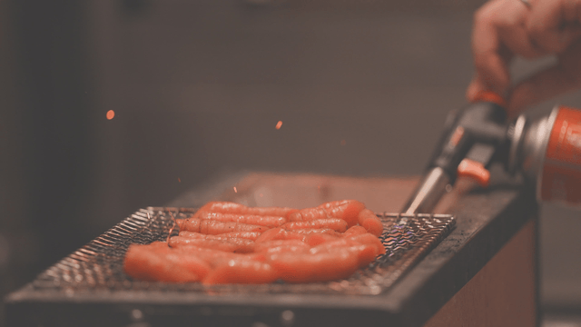 Blowtorch igniting charcoal under grill with carrot on top