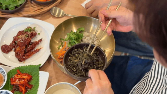 Person making bibimbap with various side dishes