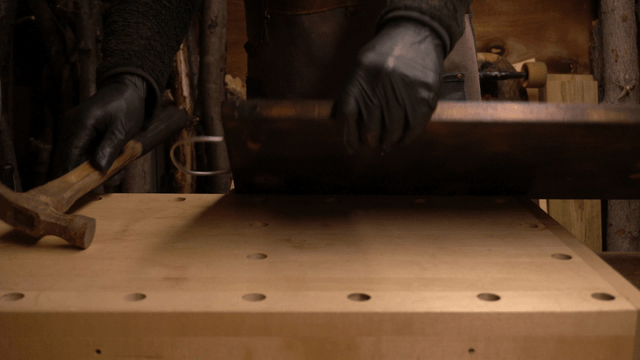 Artisan fastening metal wire onto wooden board with hammer