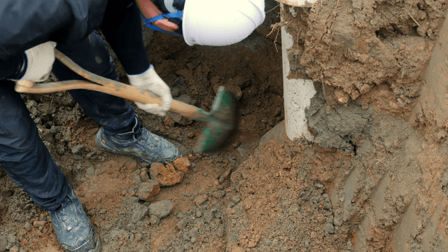Worker digging soil near a pipe