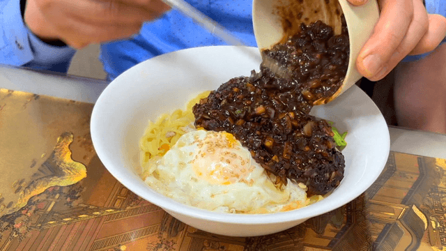 Pouring sauce over jjajangmyeon topped with fried egg