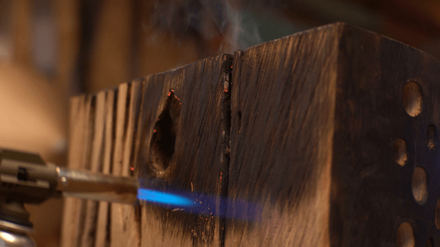 Artisan charring the surface of wooden sculpture with torch