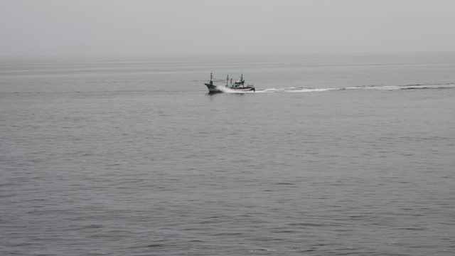 Fishing boat sailing on calm sea under cloudy sky