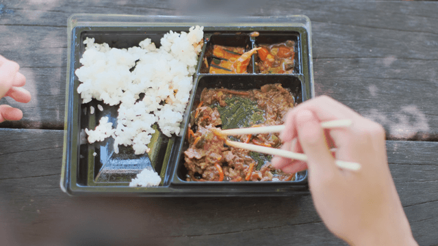 Person eating a Korean lunchbox outdoors
