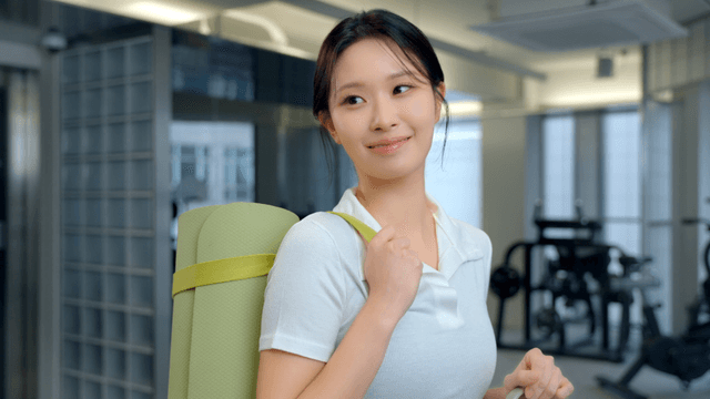 Woman smiling with a yoga mat in a gym