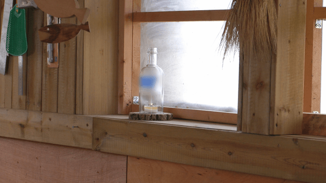 Candle in a glass bottle on wooden window frame