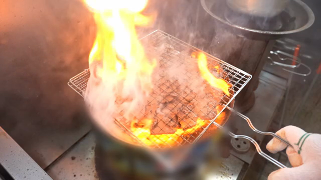 Grilling meat over open flames with smoke