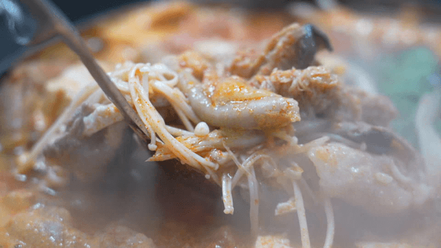 Ladle serving beef intestine stew with tofu and vegetables