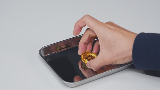A hand picking up a bitcoin from a tray