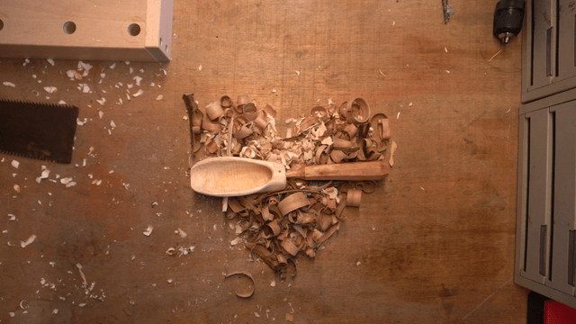 Wooden scoop placed above wooden shavings on workbench
